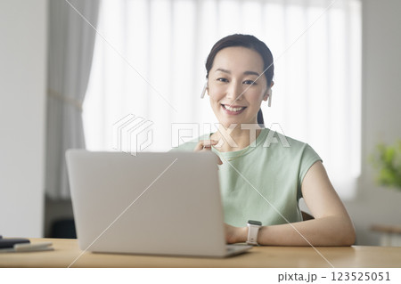 イヤホンをつけてノートパソコンに向かう30代の女性 テレワーク オンライン通話 イメージ イヤホンをつけてノートパソコンに向かう30代の女性 テレワーク オンライン通話 イメージ 123525051