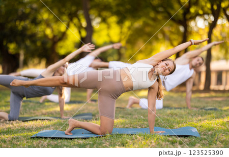 Yoga lesson visitors perform eka Padahastasana Marjariasana in park 123525390