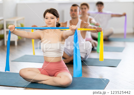 Young girl doing arm workout with band sitting cross-legged Young girl doing arm workout with band sitting cross-legged 123525442