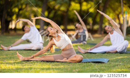 Yoga lesson visitors with coach perform Parivritta Janu Shirshasana in park Yoga lesson visitors with coach perform Parivritta Janu Shirshasana in park 123525734