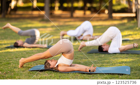 Young woman doing plow pose during group yoga in park Young woman doing plow pose during group yoga in park 123525736