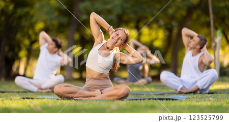 Female yoga instructor stretching in Padmasana pose with group in park 123525799