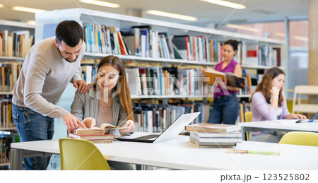 Male librarian helping focused adult student preparing to exam 123525802
