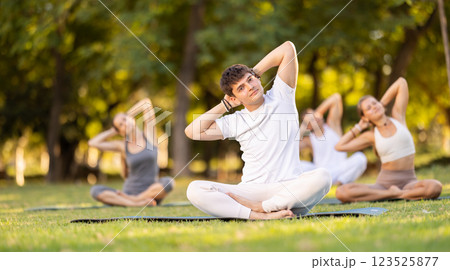 Guy stretching in lotus position during group yoga in park 123525877