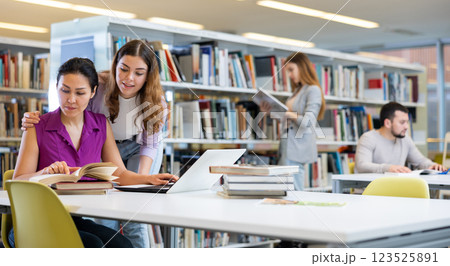 Caring woman helping friend to prepare for exams in library Caring woman helping friend to prepare for exams in library 123525891
