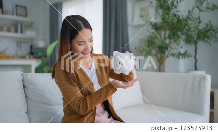 Young Asian woman putting coin in piggy bank. Save money and financial investment Young Asian woman putting coin in piggy bank. Save money and financial investment 123525913