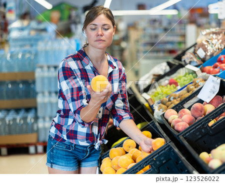 Portrait of young female choosing fresh peaches on supermarket Portrait of young female choosing fresh peaches on supermarket 123526022