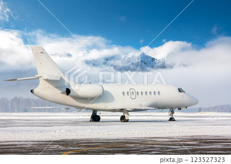 White luxury business jet on the winter airport apron on the background of high scenic mountains on a clear sunny day 123527323