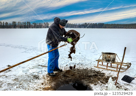 Through ice hole, farmer harvests unconsolidated sludge sapropel with pole mounted basket organic matter goes into tank, sled carries it for organic farming. Through ice hole, farmer harvests unconsolidated sludge sapropel with pole mounted basket organic matter goes into tank, sled carries it for organic farming. 123529429