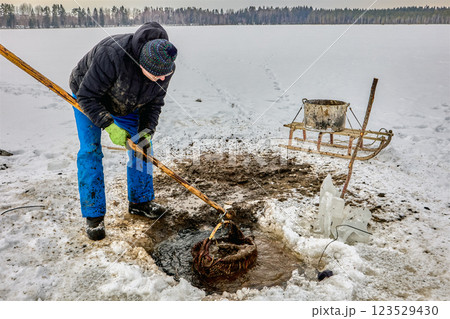 Farmer extracting sapropel from a freshwater lake through an ice hole, using a basket and sled, for use as organic fertilizer. Farmer extracting sapropel from a freshwater lake through an ice hole, using a basket and sled, for use as organic fertilizer. 123529430