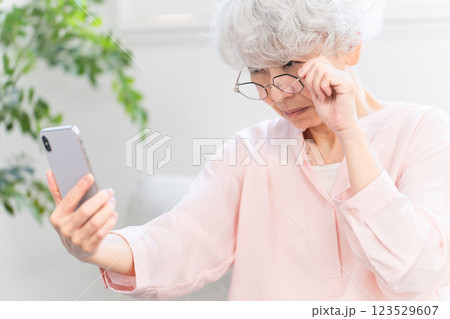 老眼でスマートフォンを見るのに苦労しているシニア女性 123529607