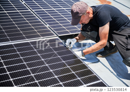 Worker building solar panel system on metal rooftop of house. Man engineer installing photovoltaic solar module outdoors. Alternative, green and renewable energy generation concept. Worker building solar panel system on metal rooftop of house. Man engineer installing photovoltaic solar module outdoors. Alternative, green and renewable energy generation concept. 123530814