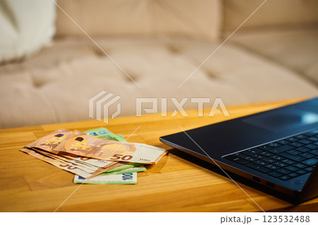 Euro banknotes and laptop on wooden table Euro banknotes and laptop on wooden table 123532488