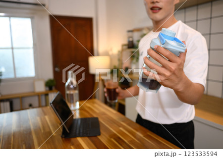 Man in white sports shirt preparing a protein shake in a stylish kitchen Man in white sports shirt preparing a protein shake in a stylish kitchen 123533594
