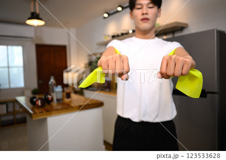Close up of young man exercising with resistance band in cozy home Close up of young man exercising with resistance band in cozy home 123533628