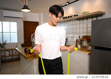 Young asian man exercising with a resistance band in a stylish kitchen Young asian man exercising with a resistance band in a stylish kitchen 123533629