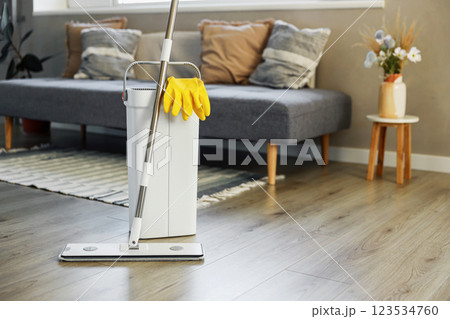 Cleaning supplies: mop, gloves, bucket with wringer sitting on wooden laminate floor in modern living room, wet equipment tools, housekeeping concept. Emphasizing home sanitation, cleanliness, hygiene 123534760