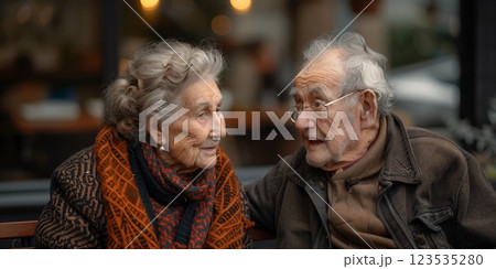 Elderly couple sitting together, smiling and sharing a heartfelt conversation, showcasing love, companionship, and warmth in an outdoor setting 123535280