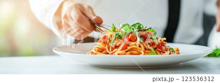 Chef garnishing fresh pasta with herbs in a bright modern kitchen during the day 123536312