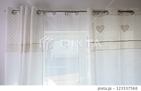 Vintage white curtains on metal rings on natural material with embroidered hearts at home. Cleaning and cleanliness. Interior and textiles.  123537568