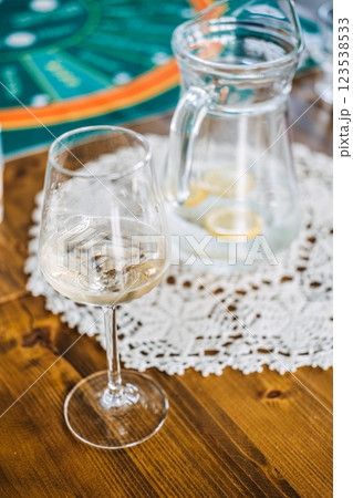 Glass of white wine and pitcher of water with lemon slices on a wooden table, set against a casino-themed game mat Glass of white wine and pitcher of water with lemon slices on a wooden table, set against a casino-themed game mat 123538533