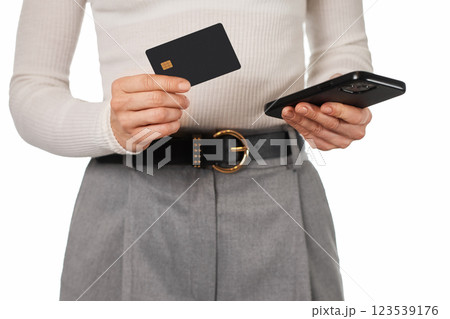 woman in white shirt holding mobile phone and black premium credit bank card on white background. Online shopping. 123539176