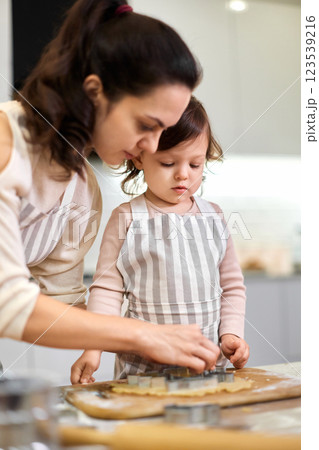 Happy family mother and little child daughter cutting cookies of raw gingerbread dough in kitchen 123539216