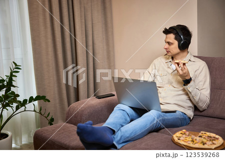 man sitting on sofa and eating pizza while working on laptop man sitting on sofa and eating pizza while working on laptop 123539268
