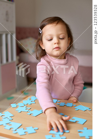 Cute little child girl connecting puzzle pieces on wooden desk in room, children development Cute little child girl connecting puzzle pieces on wooden desk in room, children development 123539328