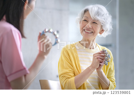 鈴を持った笑顔のシニア女性と介護スタッフ　音楽療法　アクティビティ　イメージ 123539801