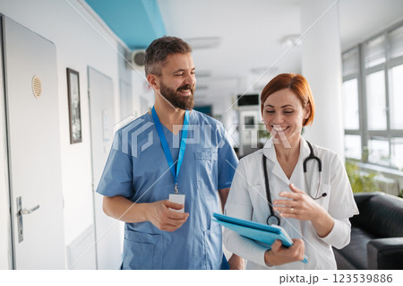 Two doctors walking across hospital hallway, holding medical records in hand. Two doctors walking across hospital hallway, holding medical records in hand. 123539886