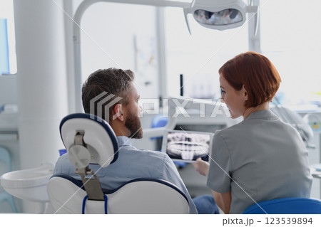 Female dentist showing x-ray to patient in dental clinic during anual check-up. Female dentist showing x-ray to patient in dental clinic during anual check-up. 123539894