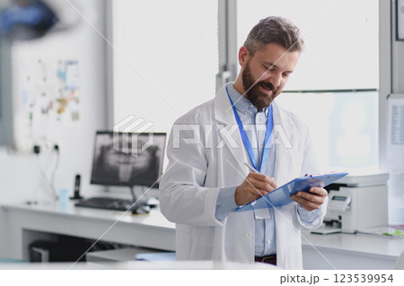 Doctor in doctors office reading medical records in clipboard. 123539954