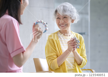 鈴を持った笑顔のシニア女性と介護スタッフ　音楽体操　音楽療法　アクティビティ　イメージ 123540051