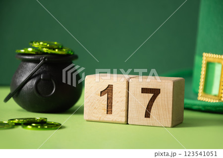 St Patricks day concept with green Leprechaun Hat, coins in black pot, celebrate date at wooden block on green background. Close up. Copy space. 123541051