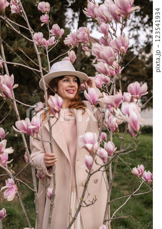 Woman magnolia flowers, surrounded by blossoming trees., hair down, white hat, wearing a light coat. Captured during spring, showcasing natural beauty and seasonal change. Woman magnolia flowers, surrounded by blossoming trees., hair down, white hat, wearing a light coat. Captured during spring, showcasing natural beauty and seasonal change. 123541934