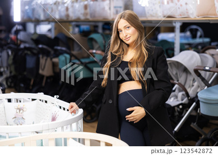 Pregnancy shopping concept. Pregnant woman choosing cradle cot or crib for newborn at baby shop store 123542872