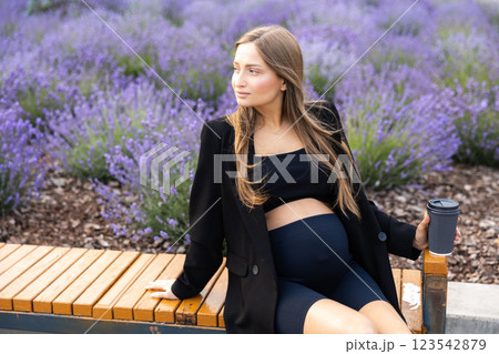 Pregnant woman sits on bench in the park holding cup of coffee 123542879