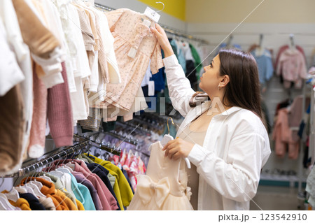 Pregnant woman choosing dress and bodysuits at clothing store. Mother doing shopping in baby shop. Baby clothes sale and pregnancy concept. Pregnant woman choosing dress and bodysuits at clothing store. Mother doing shopping in baby shop. Baby clothes sale and pregnancy concept. 123542910