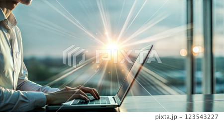 Man using a laptop in front of a bright sunburst through a large window symbolizing new beginnings and opportunities Man using a laptop in front of a bright sunburst through a large window symbolizing new beginnings and opportunities 123543227