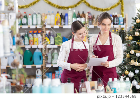 Woman seller with teen daughter, using paper report make inventory in household chemistry store 123544369