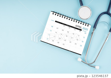 April 2025 desk calendar and stethoscope on blue, Position with copy space. April 2025 desk calendar and stethoscope on blue, Position with copy space. 123546137
