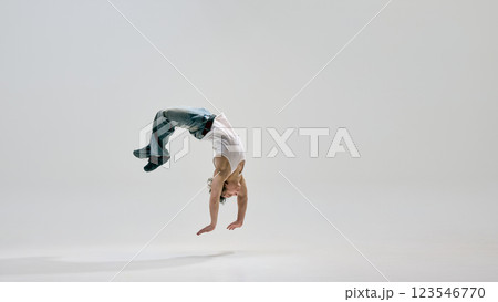 Dancer, dressed casual clothes, arching backwards mid-air, frozen in moment of flight and precision against white background. 123546770