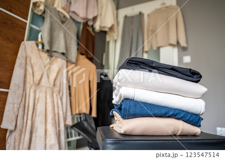 Stacked pile of clothing prepared for resale, donation, or recycling, with wardrobe with outfits in the background. Sustainable fashion choices help reduce waste and support a circular economy 123547514