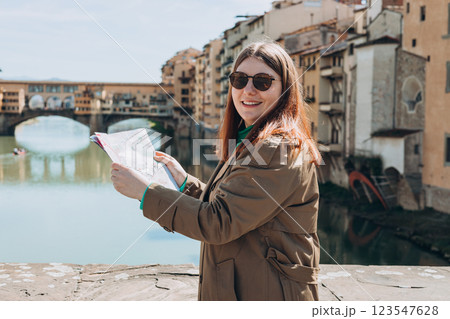 Beautiful 30s woman standing with paper map on famous Old bridge in Florence. Traveling Europe in summer. Attractive female is exploring city. Top tourist attraction 123547628