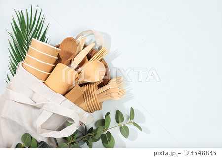 A set of environmentally friendly dishes in an eco bag on a sunny table. Paper cups, plates, kraft paper napkins, barbecue straws, wooden forks, spoons and knives, mockup, healthy lifestyle concept, 123548835