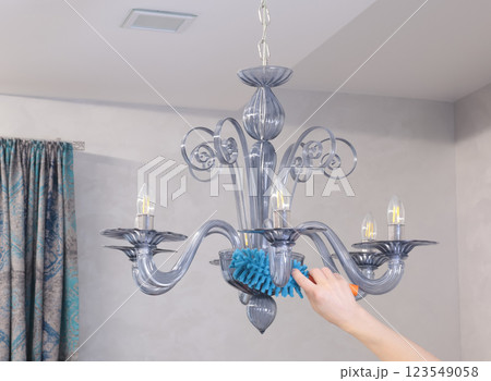 Woman wipe dust on glass chandelier with fluffy broom in living room. Cleanliness and order.  123549058