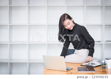 Asian businesswoman sitting on the edge of desk and working in modern office. Asian businesswoman sitting on the edge of desk and working in modern office. 123549235