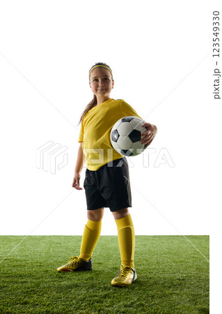 Confident girl, child in yellow jersey and black shorts proudly standing with soccer ball against white studio background. Champion Confident girl, child in yellow jersey and black shorts proudly standing with soccer ball against white studio background. Champion 123549330