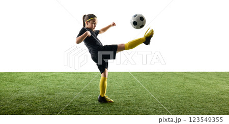 Child, girl in black uniform playing soccer, training, kicking ball with outstretched leg while standing on grassy surface against white background Child, girl in black uniform playing soccer, training, kicking ball with outstretched leg while standing on grassy surface against white background 123549355